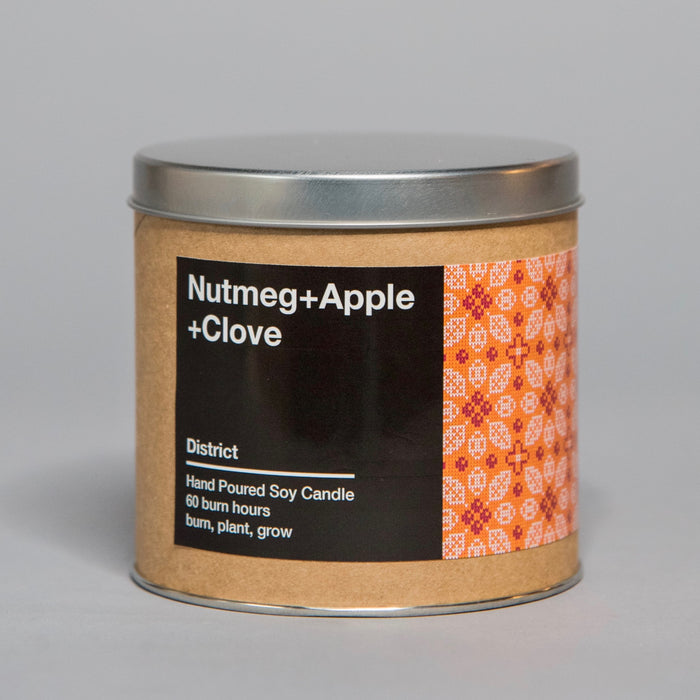Hand poured soy candle with nutmeg, apple, and clove scent in a brown container with a metal lid and decorative label