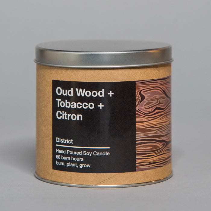 Hand poured soy candle with oud wood, tobacco, and citron scent in a tin container with wood grain design label