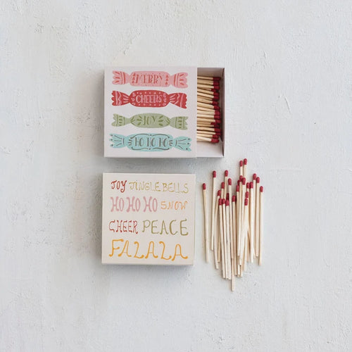 Holiday-themed matchboxes with red-tipped matches, featuring festive phrases and designs on a white background.