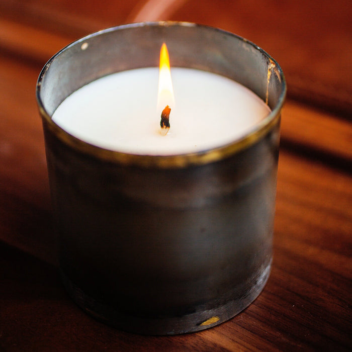 Lit white candle in a rustic metal container on a wooden surface for cozy home decor ambiance