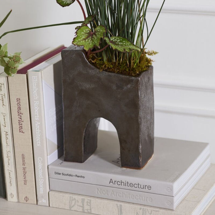 Dark grey sculptural bookend holding books and supporting a small planter with green plants on a shelf