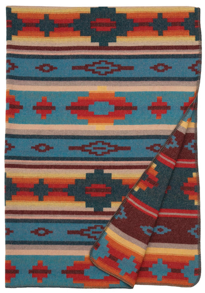 Folded wool blanket with vibrant southwestern geometric patterns in blue, red, orange, and beige tones.