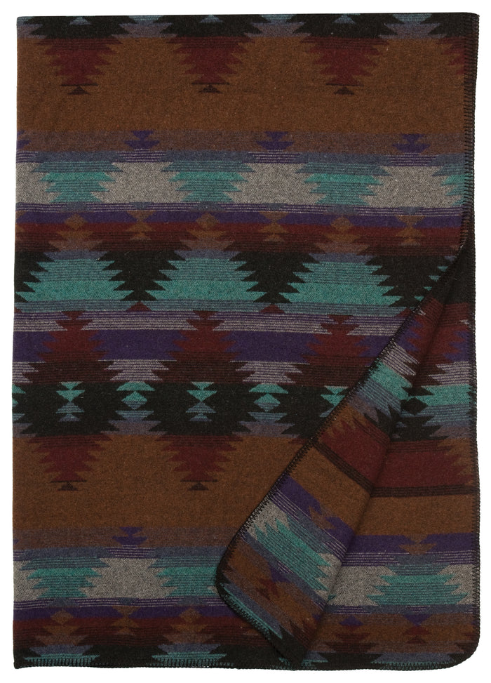 Folded wool blanket with earthy tones and geometric southwestern pattern in teal, brown, gray, and purple.