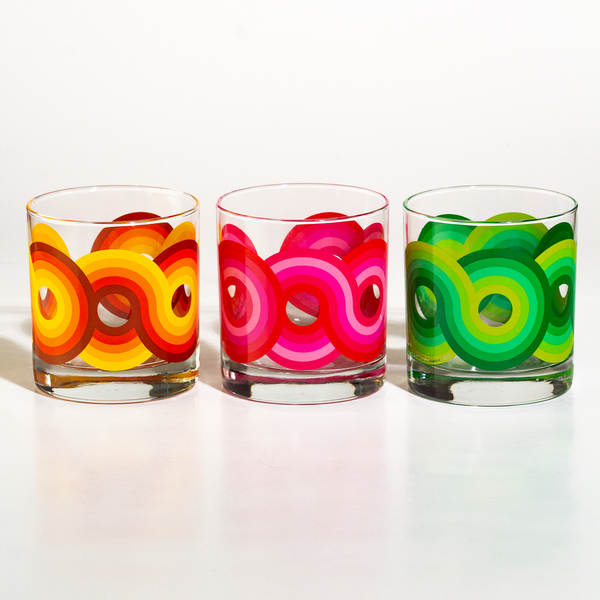 Set of three colorful patterned rocks glasses with orange, pink, and green circular designs on clear glass